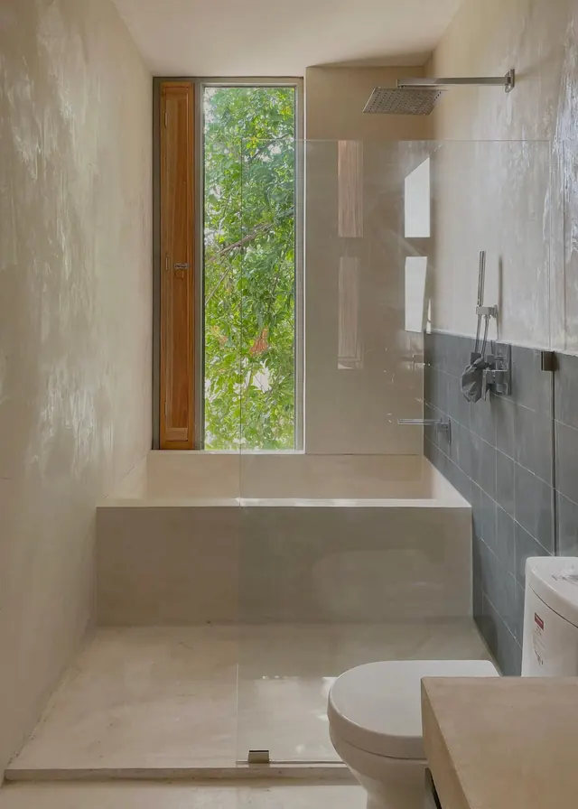 Bathroom in polished plaster with a built-in tub and a tall window onto the trees