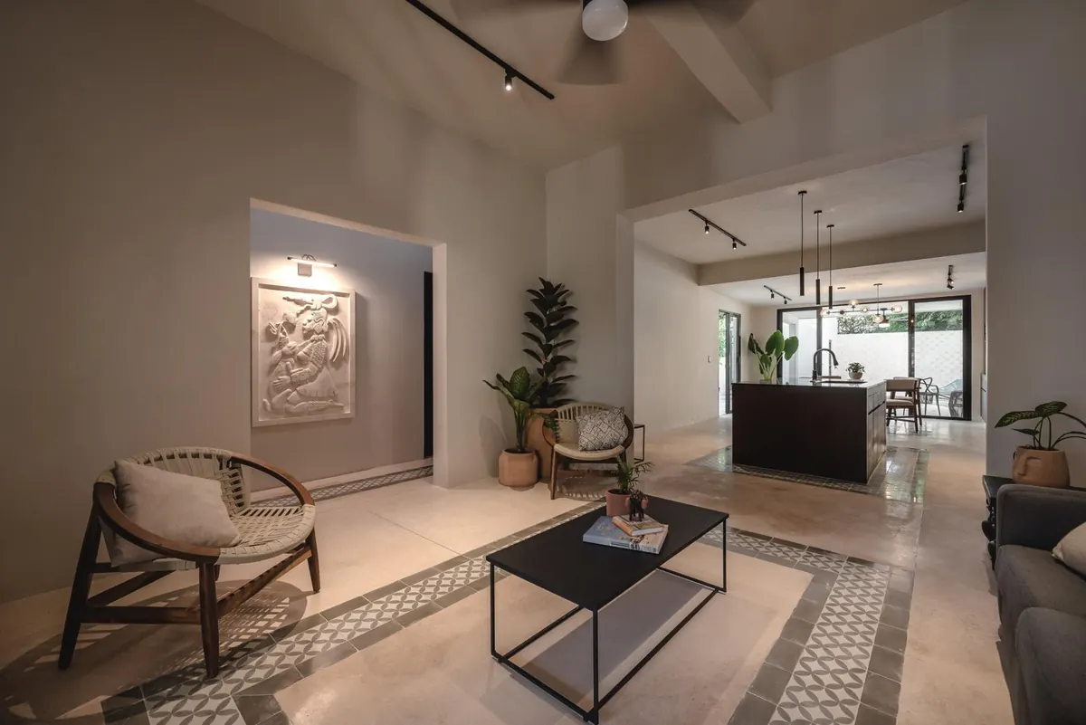 Living room with cement-tile inlays, woven armchairs and a carved stone panel, open to the kitchen