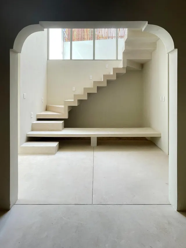 Cantilevered stair under a clerestory window, seen through an arched opening