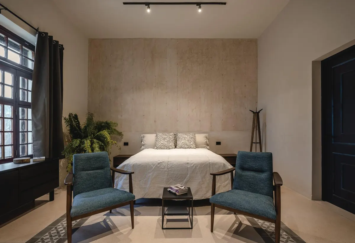 Main bedroom with plaster feature wall, two blue armchairs and a street-facing window